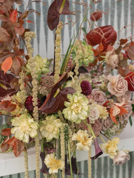 Wedding floral arrangement with ceremony floral installation of anthurium, roses, dahlias and hanging amaranthus against a corrugated metal wall