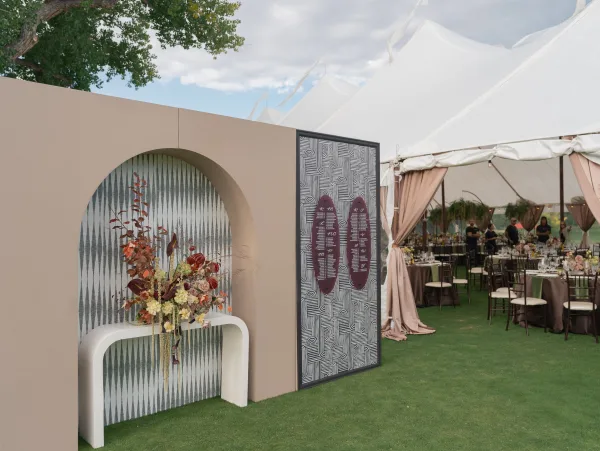 Reception entrance decor with wedding seating chart display on a curved console table, statement floral arrangement, arched backdrop, and tent string lights