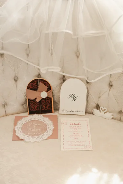 Invitation suite wedding invitation flat lay with RSVP and details cards, envelope, wax seal and ribbon bow on a tufted sofa backdrop