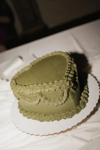 Wedding cake in a heart shaped design with vintage piped frosting on a scalloped board, set on a tablecloth with upholstered seating behind
