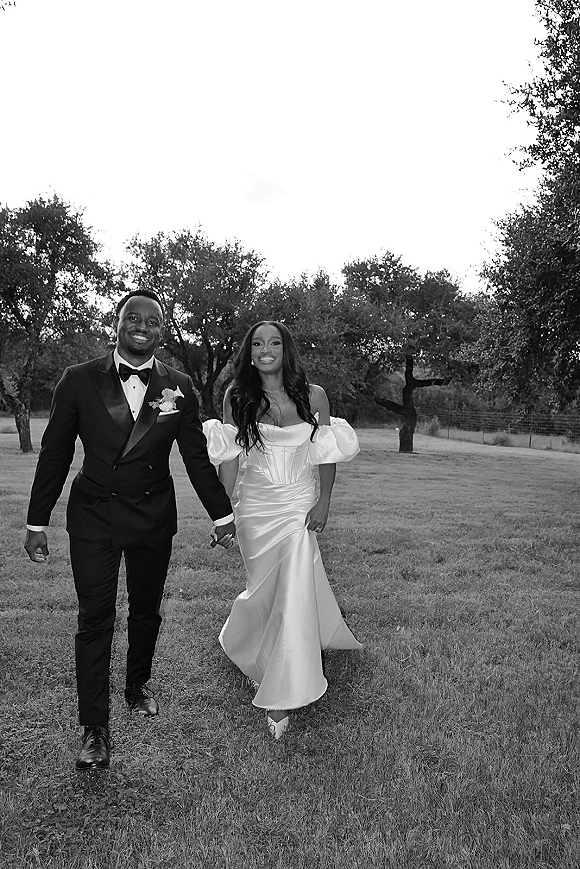 Couple portrait in a black and white wedding portrait, bride in a wedding dress and groom in tuxedo holding hands in a grassy field