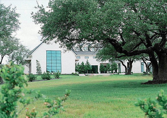 Wedding venue exterior of a modern wedding venue with white facade, large grid windows, and manicured shrubs on a green lawn under overcast skies