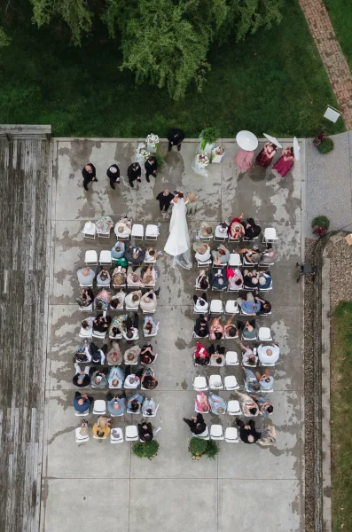 Outdoor wedding ceremony aerial photo showing bride with long train and veil walking the aisle runner as guests sit by parasol-holding bridesmaids