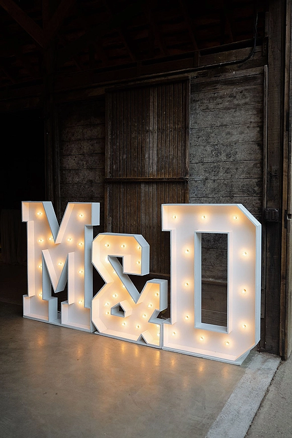 Marquee letters glowing in warm white bulbs, set before wooden barn doors on a concrete floor in a rustic interior setting
