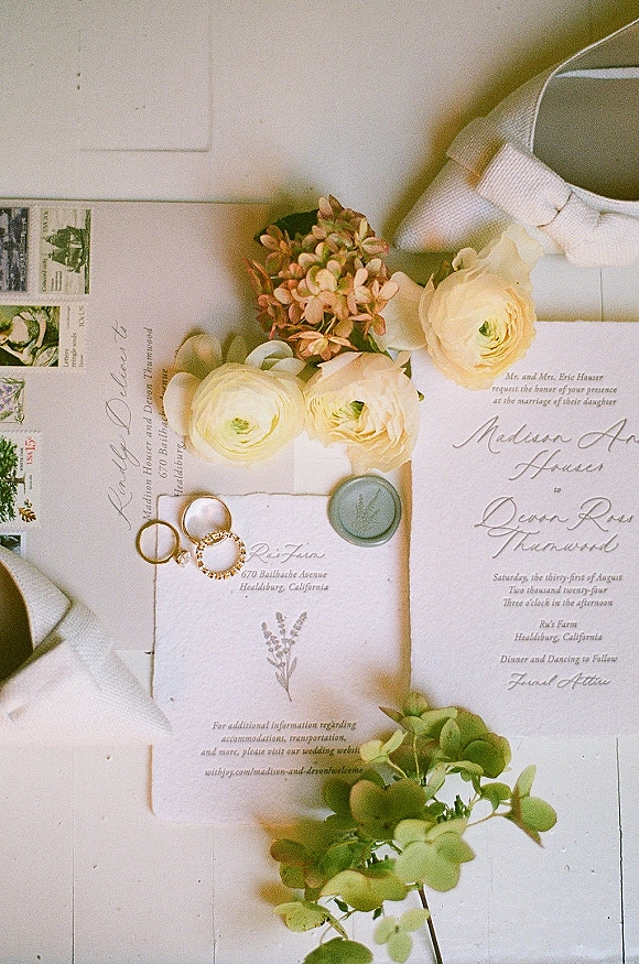 Invitation suite wedding invitation flat lay with envelopes, vintage stamps, rings and ribbon, finished with a sage green wax seal on white surface