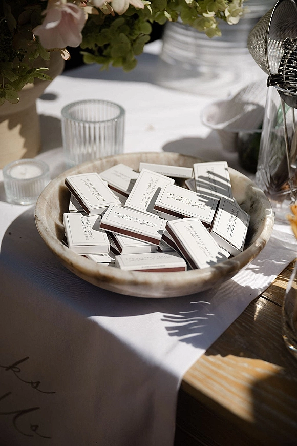 Wedding favors with personalized matchboxes wedding favor arranged in a ceramic bowl beside ribbed votive holders on a sunlit wood table