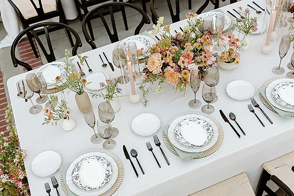 Reception tablescape with wedding table centerpiece of bud vases, taper candles and glass hurricanes on white linen at an outdoor patio reception