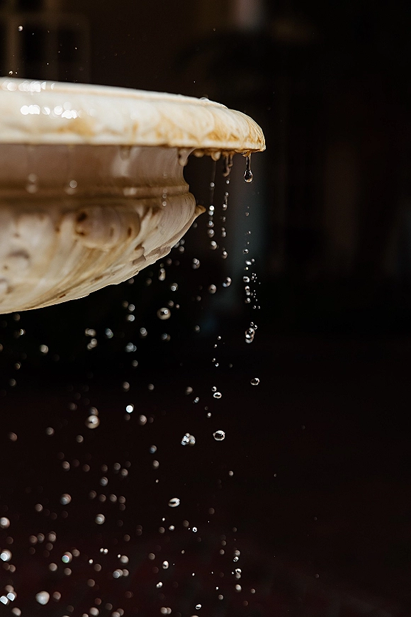 Stone fountain detail with carved rim and water droplets dripping over the edge against a dark, moody background