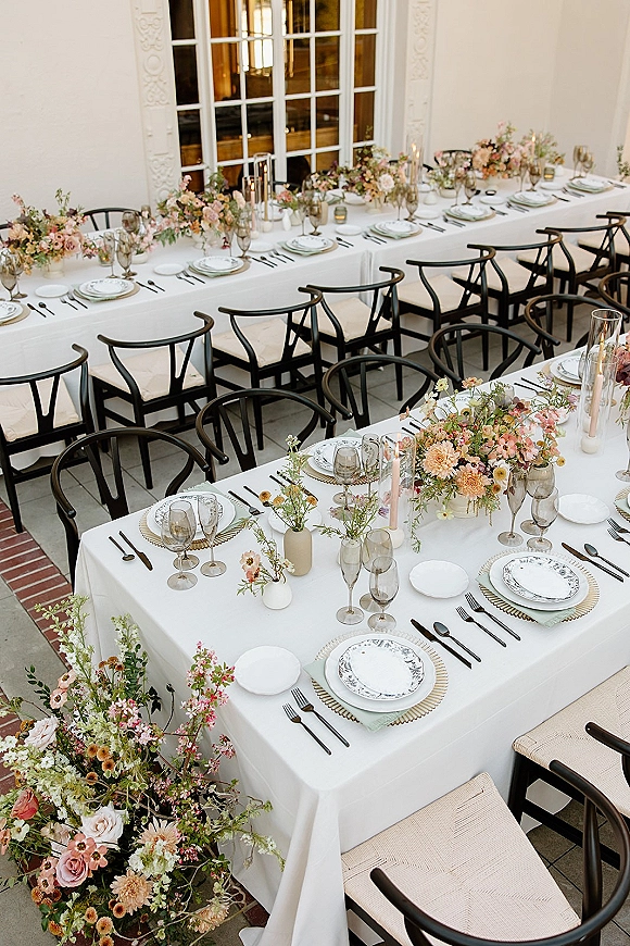 Reception tablescape with a long table wedding reception setup, pastel floral centerpieces in bud vases with taper candles by large windows
