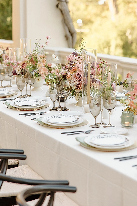 Reception tablescape with pastel wedding tablescape florals, taper candles, and patterned plates on a sunlit outdoor terrace with stone railing