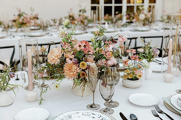 Reception tablescape with wedding table centerpiece, lush floral centerpiece and blush taper candles on white linens by window panes