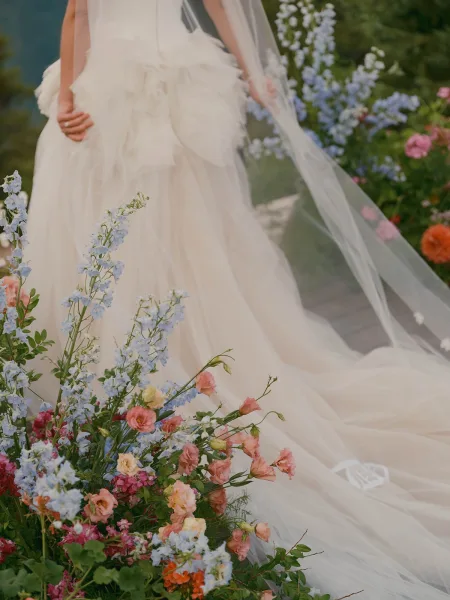 Wedding dress with tulle wedding gown ruffles and long veil train trailing on a garden walkway, framed by greenery and soft flowers