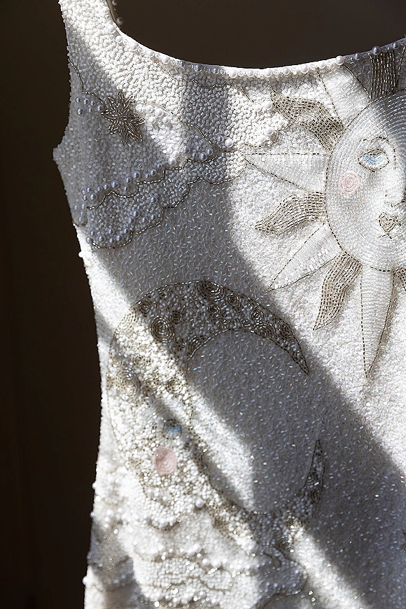Wedding dress close-up showing beaded wedding dress embroidery with pearls and sequins shimmering against a dark backdrop