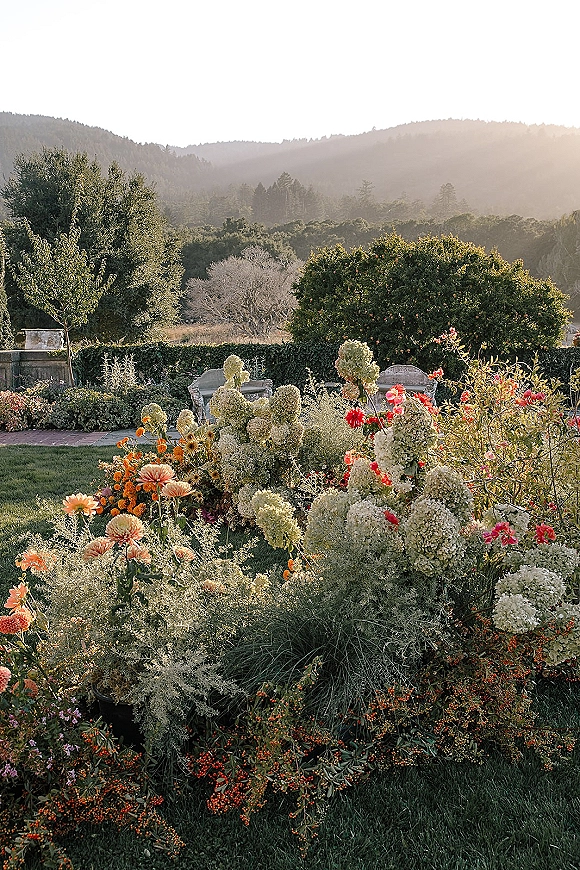 Garden wedding florals with hydrangeas, dahlias, and roses lining a brick path to bench seating, set against hazy mountain views