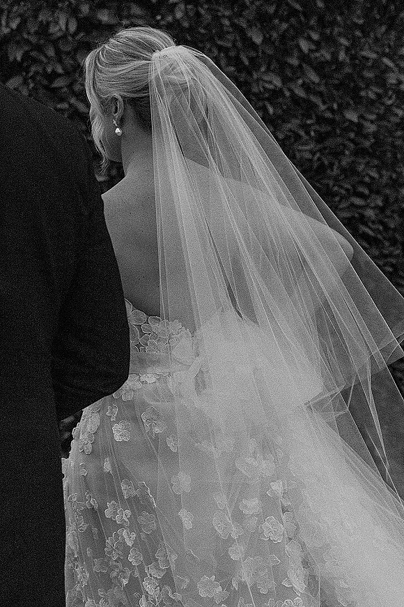 Wedding veil portrait of a bride from behind, looking over her shoulder in a black and white wedding portrait with lace dress and pearl earrings