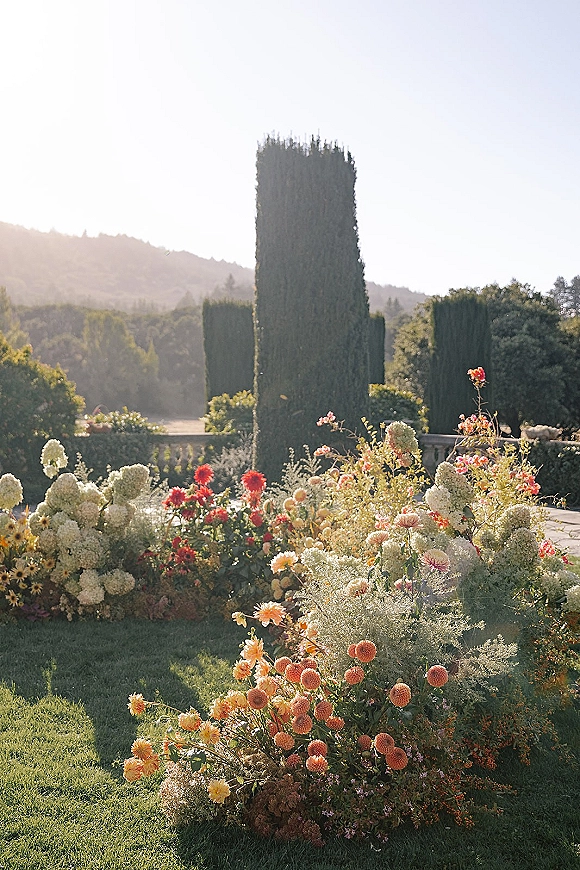 Wedding floral meadow with ceremony ground florals of hydrangea, dahlias, and wildflowers lining a stone terrace by cypress trees