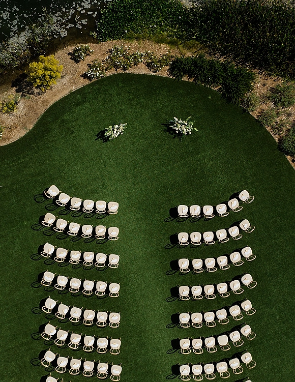 Ceremony seating layout with outdoor ceremony seating in a curved semi-circle of white chairs, with floral arrangements on a green lawn path