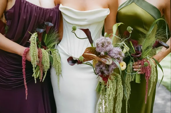 Bridesmaid bouquets featuring cascading hanging amaranthus, carried by the bridal party against lush garden greenery along a walkway.