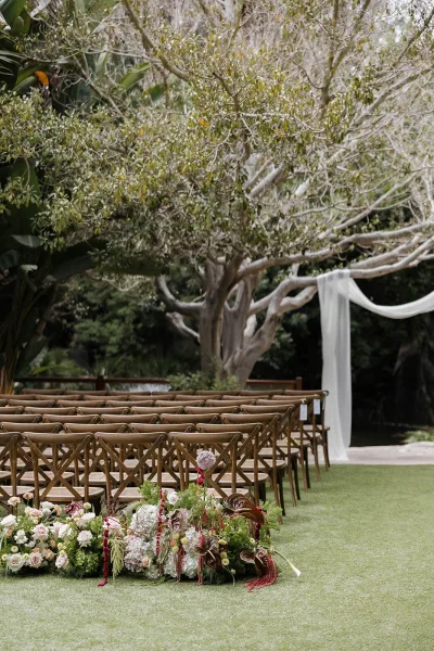 Ceremony setup with garden ceremony decor, rows of wooden chairs arranged on a lush lawn beneath garden trees framing the natural backdrop.
