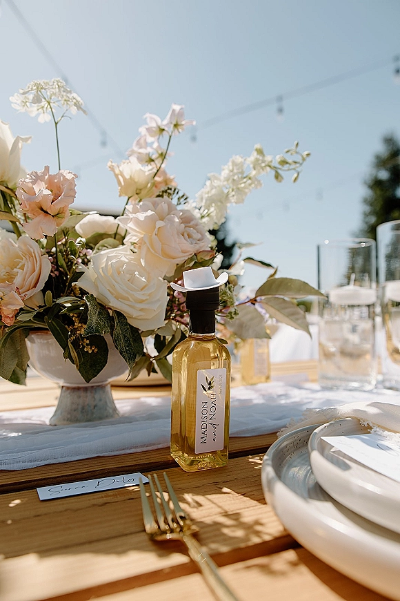 Reception tablescape with wedding table centerpiece of blush roses and greenery, place cards and gold flatware under string lights outdoors