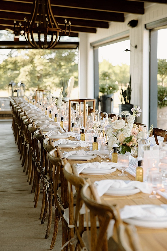 Reception tablescape with long banquet table wedding styling, lantern florals and votive candles under a chandelier on a covered patio