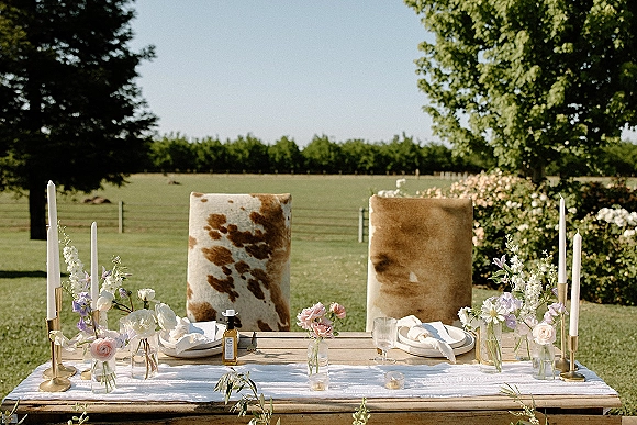 Reception tablescape with outdoor wedding table styling, white runner and brass taper candles on a wood farm table on a grassy pasture lawn