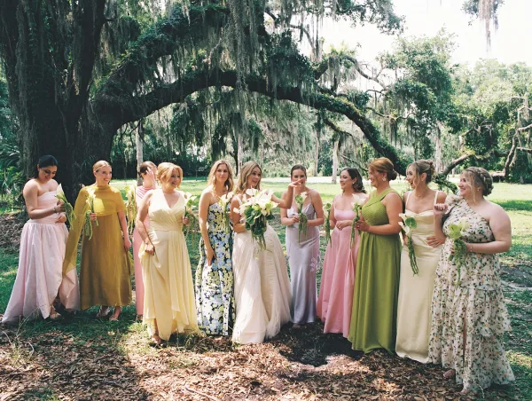 Bridesmaid group photo of the bride with bridesmaids in pastel mismatched dresses holding calla lily bouquets under an oak tree with hanging moss