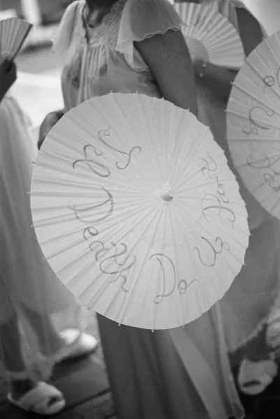 Wedding parasols with personalized calligraphy lettering and ribbon bows held by bridesmaids and guests along an outdoor walkway