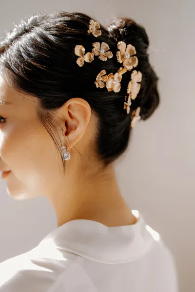 Bridal hair accessory with gold floral hair pins framing a sleek updo, highlighting the delicate floral design and luminous finish.