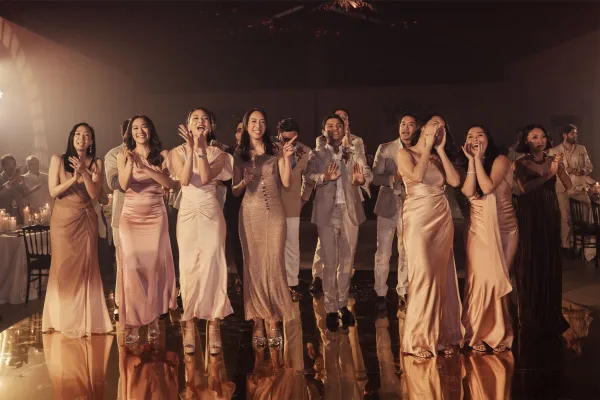 Wedding party reaction as wedding guests cheer, bridesmaids in satin beam beside groomsmen at a candlelit indoor reception