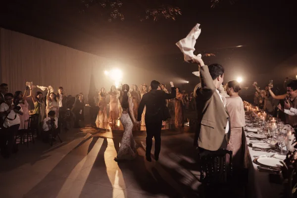 Wedding reception entrance as the newlyweds hold hands in a wedding grand entrance, guests waving napkins under stage lights on the dance floor.