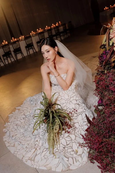 Bridal portrait of a bride holding a bouquet amid candlelit reception tables and draped curtains, with modern black chairs in view.
