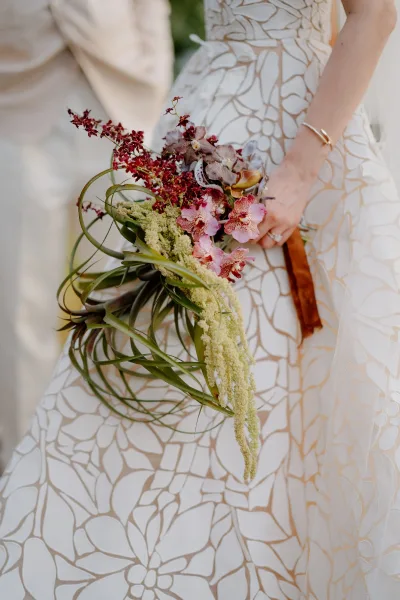 Bridal bouquet, a cascading bridal bouquet featuring orchids, cradled against patterned gown fabric.