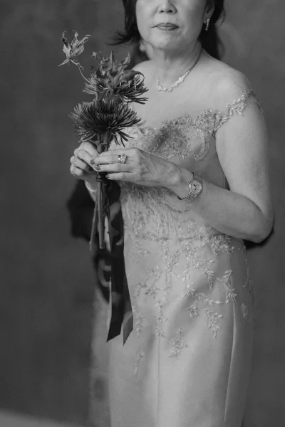 Wedding portrait in black and white of a woman holding a small ribbon-tied bouquet, hands gently cradling the stems with calm poise.