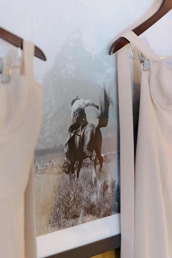 Wedding dress details on a bridal gown on hanger with clean neckline and straps, set against a white wall with framed art