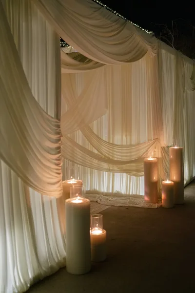 Draped wedding backdrop styled as a wedding curtain backdrop, glowing with candles against a night sky with silhouetted tree branches.