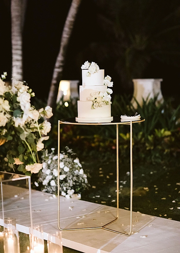 Wedding cake three tier wedding cake on a gold stand with white sugar flowers, candles and florals in a night-lit garden setting