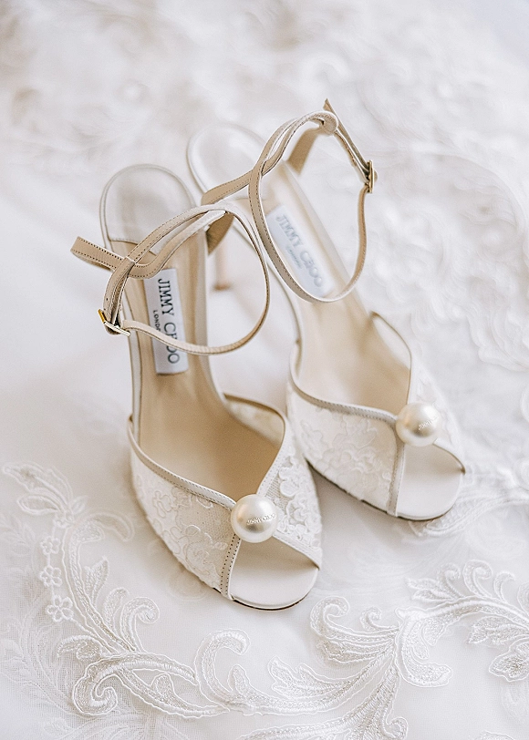 Bridal shoes with pearl wedding heels styling, lace overlay and ankle straps, arranged on embroidered lace fabric for detail shot