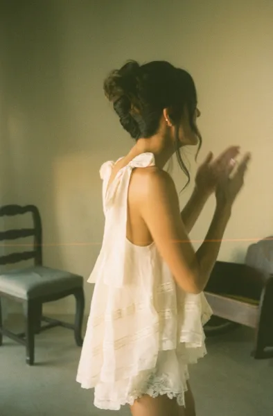 Bridal portrait of a bride in a short wedding dress, adjusting her wedding ring in soft window light beside a mirror indoors