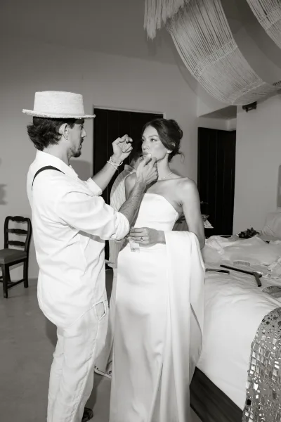Bridal makeup touch-up during wedding getting ready, bride in a strapless dress with earrings and ring in a hotel room