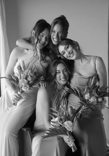 Bridesmaids portrait with bridesmaids group photo holding bouquets in mismatched satin dresses, posed indoors beside a curtain and chair
