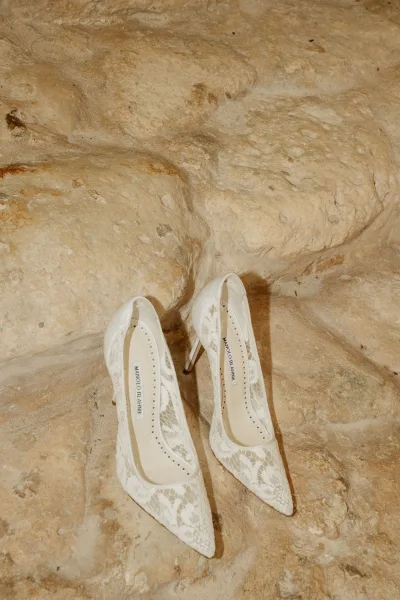 Bridal shoes, lace wedding heels in white lace pointed-toe pumps arranged as a flat lay on a textured stone surface