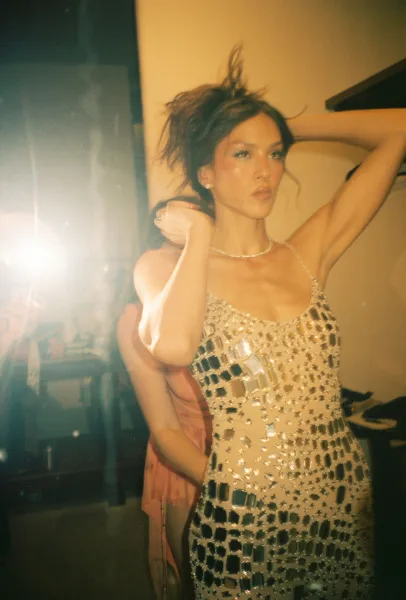 Bridal portrait of a bride in a beaded spaghetti-strap gown adjusting her updo, crystal necklace sparkling in warm mirror-lit room