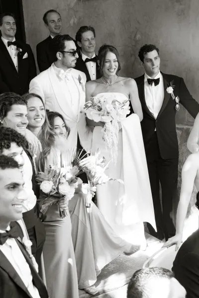 Wedding party photo of bride holding a bouquet with bridesmaids and groomsmen in tuxedos on stone steps by a stucco wall