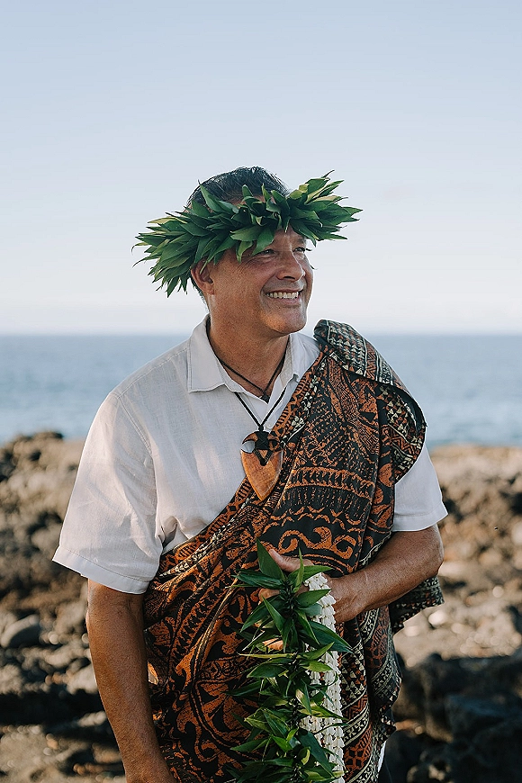 Wedding officiant holding a lei garland in a wedding officiant portrait, wearing a leaf crown on an oceanfront rocky shoreline