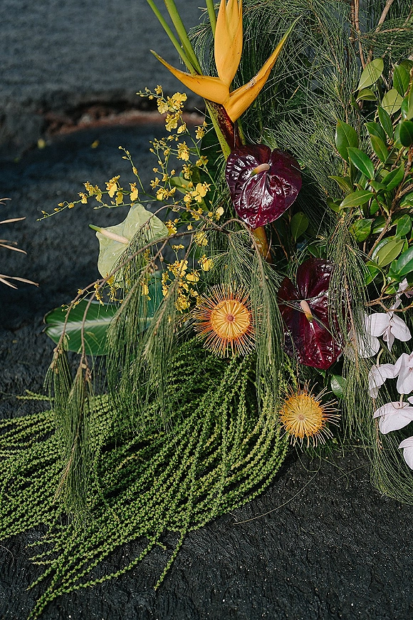 Wedding floral arrangement of tropical wedding flowers with bird of paradise, anthurium, orchids, and greenery on a dark stone surface
