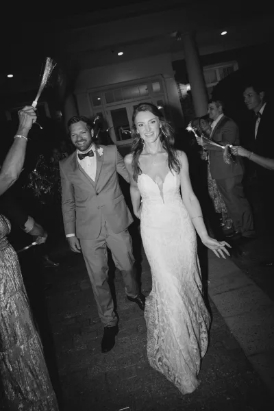 Wedding send off as bride and groom walk through a sparkler exit tunnel, guests lining steps by a columned entrance at night