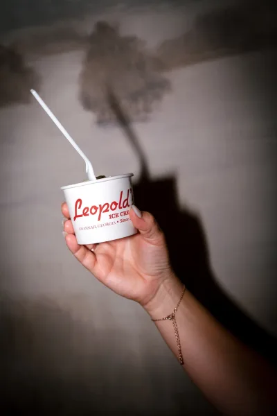 Wedding ice cream in a white dessert cup with spoon, held by a hand with ring and bracelet against a wall with soft shadows
