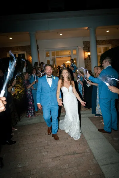 Wedding send off as bride and groom walk hand in hand through cheering guests with fiber optic wand lights on a brick walkway at night