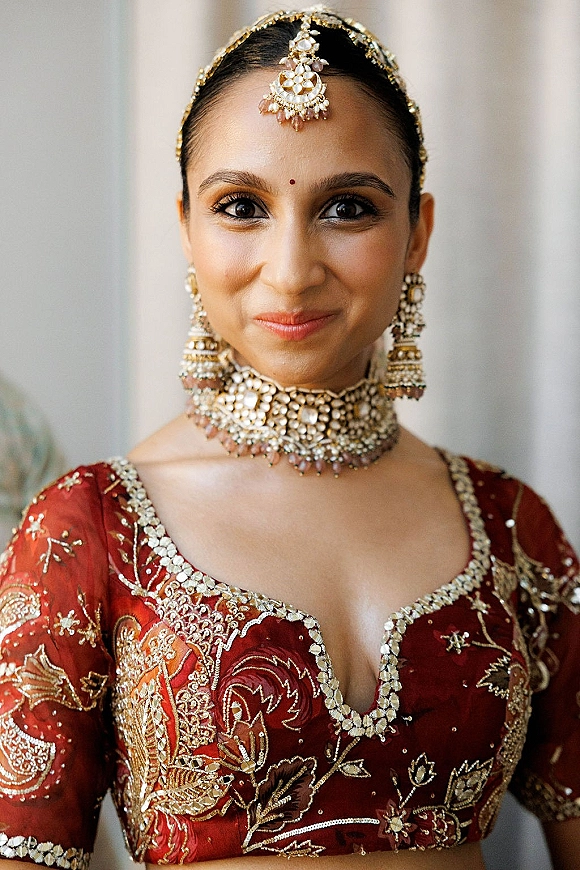 Bridal portrait of an Indian bride portrait wearing a maang tikka accent, chandelier earrings, and choker necklace in soft indoor light